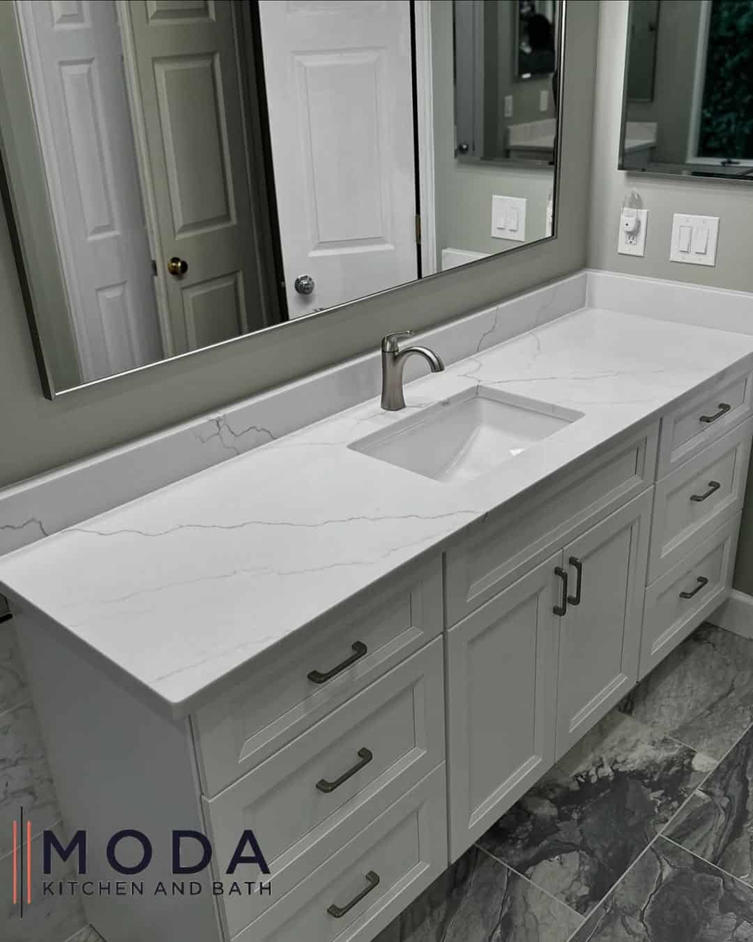 White shaker bathroom vanity with wide veined quartz countertop, undermount rectangular sink, brushed nickel faucet, and gray marble-look tile floor