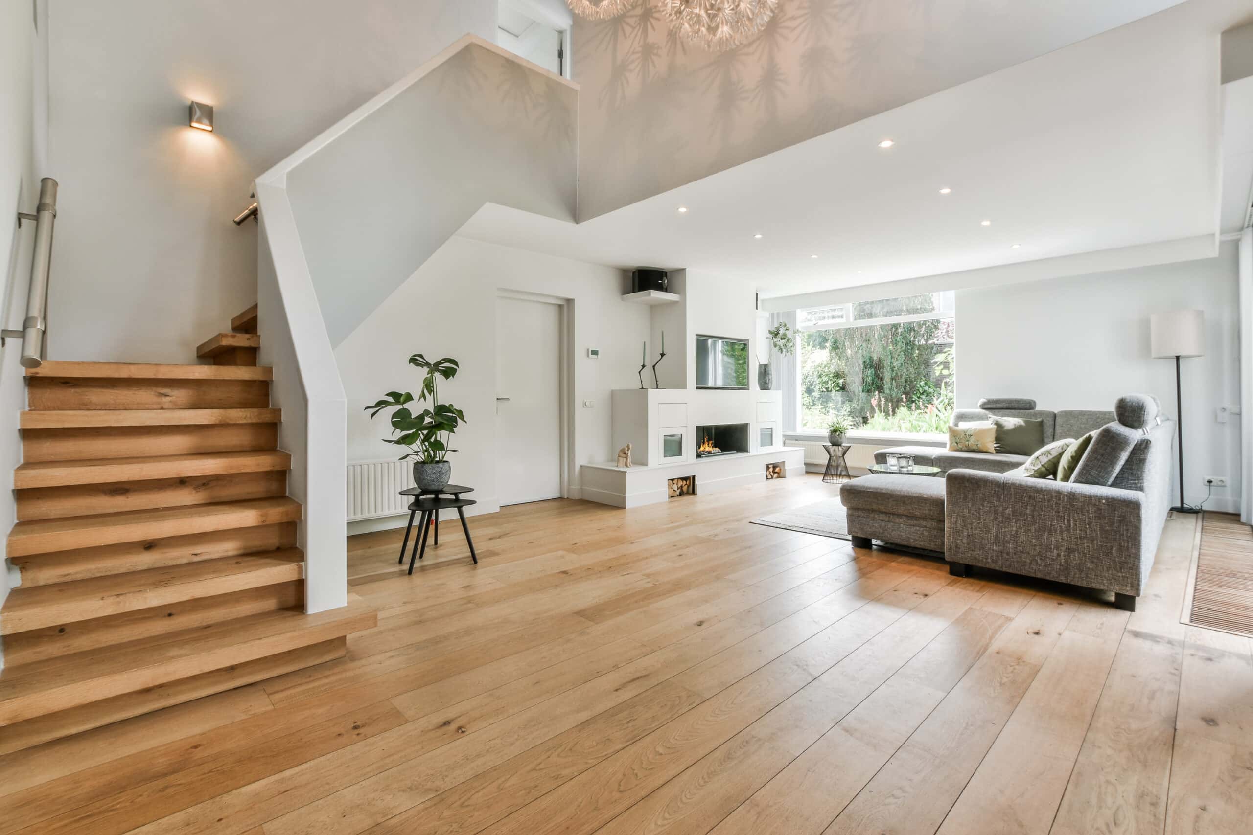 Wide-plank hardwood flooring installation in open-concept living room with oak staircase, fireplace, and high ceilings in Northern Virginia home