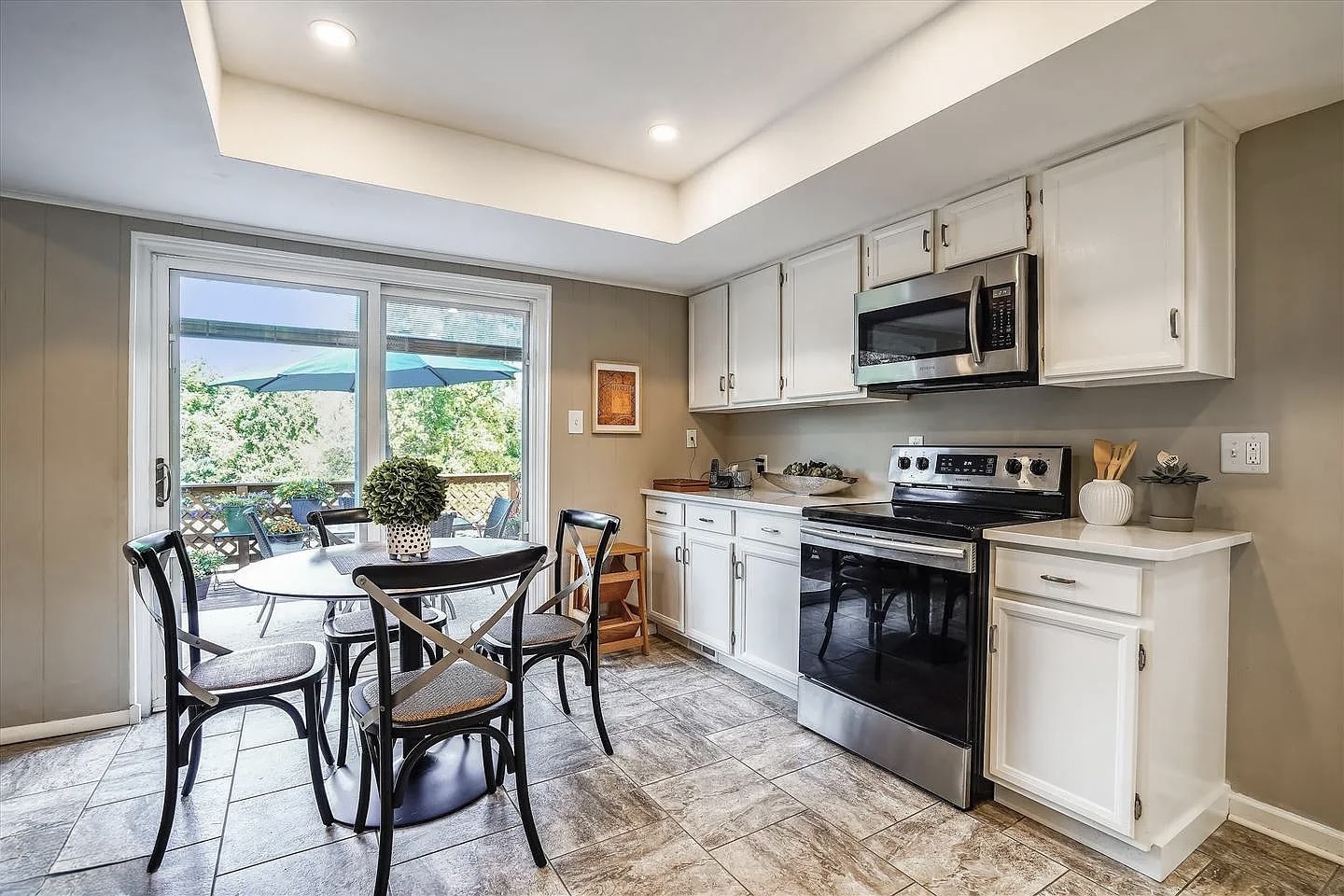 Kitchen before remodeling with white upper cabinets, gray porcelain tile floor, sliding glass door to patio, and small dining table