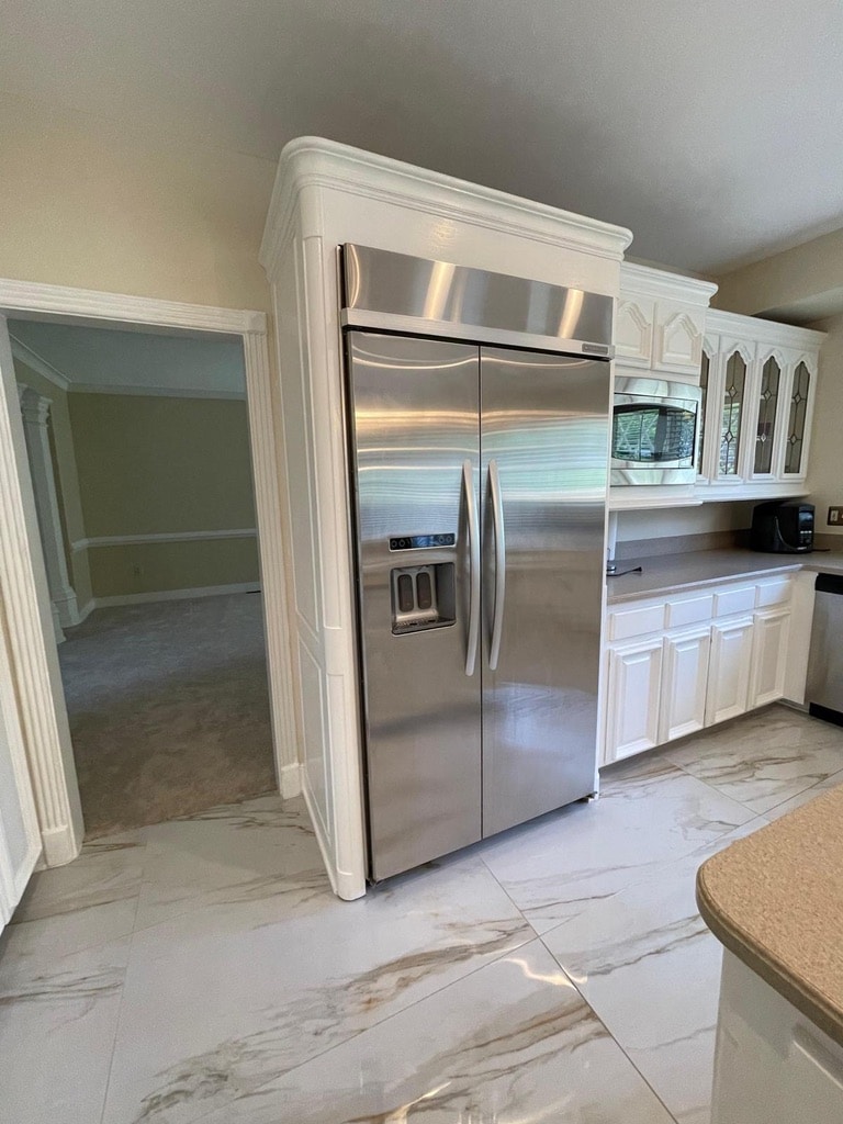Remodeled kitchen showing built-in stainless side-by-side refrigerator with white crown molding cabinet surround and large-format marble-look porcelain tile floor