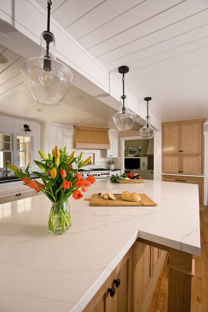 Open kitchen remodel featuring large quartz waterfall island, natural oak cabinets, shiplap ceiling, and glass pendant lights over hardwood floors