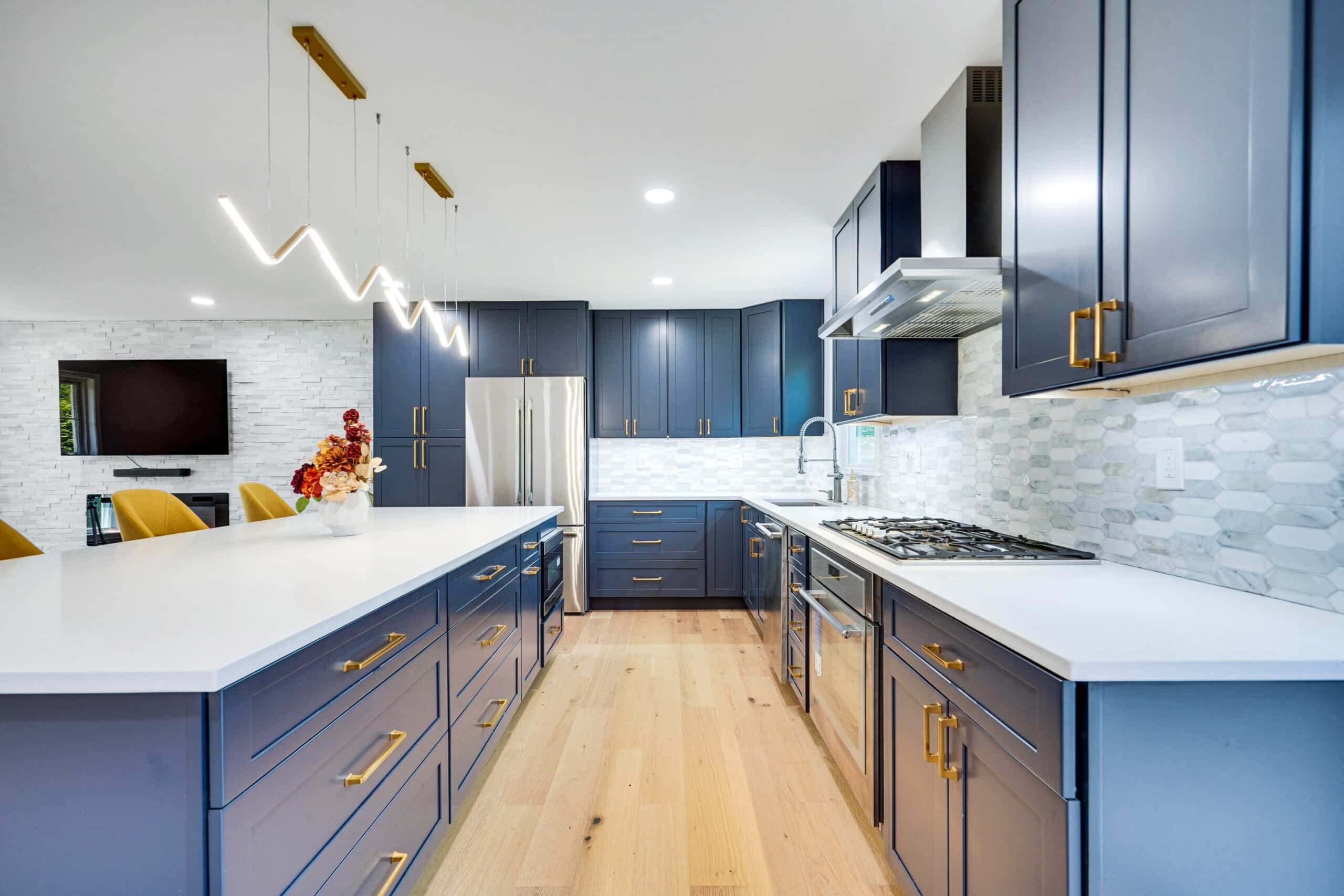 Galley-style kitchen remodel with navy blue cabinets, brass bar pulls, white quartz countertops, stainless double wall oven, and wide-plank white oak hardwood floors