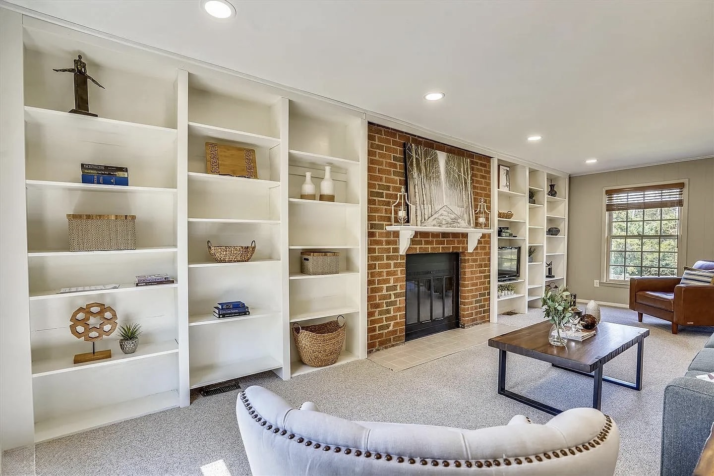 Living room before renovation showing floor-to-ceiling white built-in shelving surrounding brick fireplace and wall-mounted TV